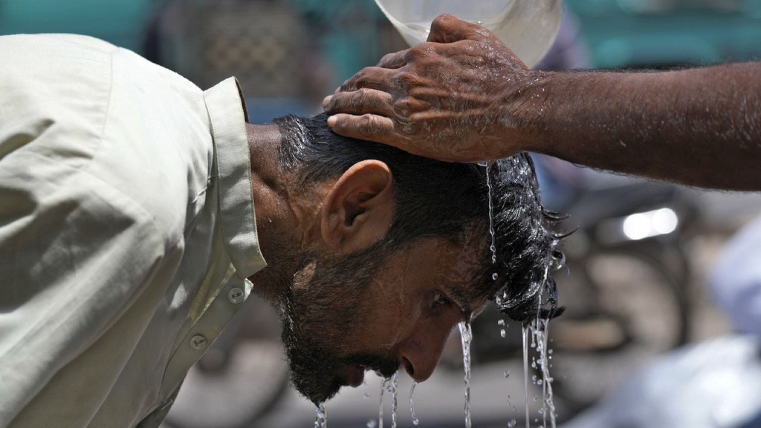 Ein Freiwilliger gießt einem Mann Wasser über den Kopf, um sich an einem heißen Sommertag in Karachi, Pakistan, abzukühlen