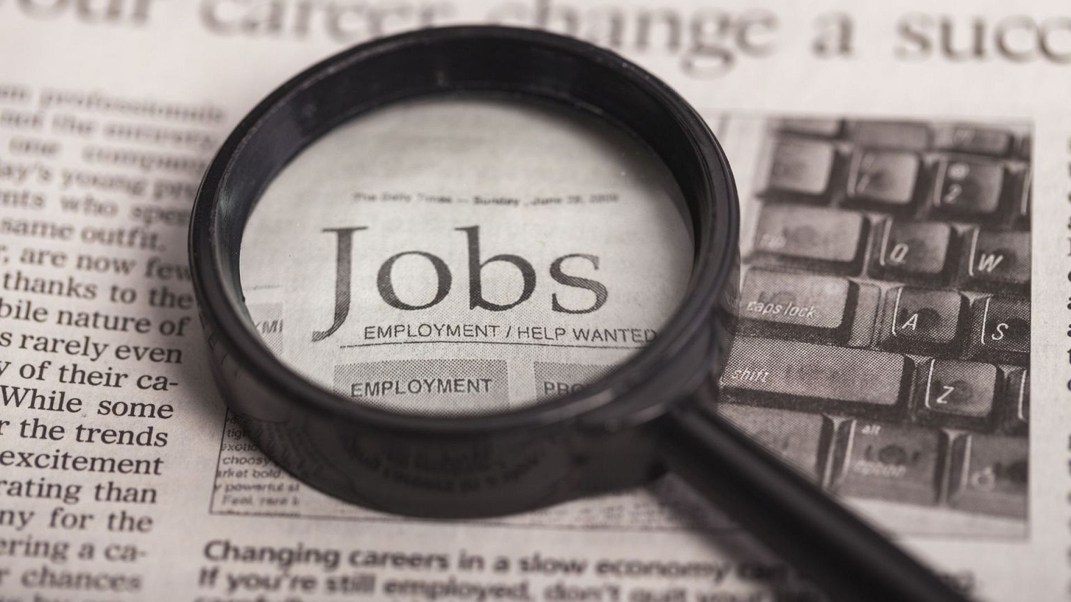 Una lupa sobre un periódico ampliando la palabra "empleo".
