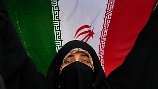 Una mujer iraní iza la bandera de su país durante una manifestación contra Estados Unidos e Israel, Irán, martes 24 de junio de 2025.  