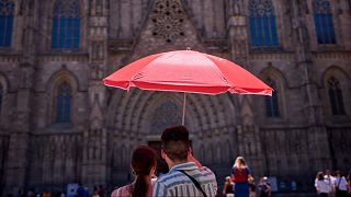 Ein Paar schützt sich mit einem Regenschirm vor der Sonne, während es die Kathedrale von Barcelona betrachtet.
