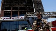 An Iraqi security guard stands in front of a mall that caught fire in Kut, 17 July, 2025